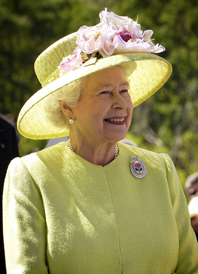 Her Majesty Queen Elizabeth II. Wearing a lime suit jacket and matching hat. With a pearl embossed brooch showing a pink rose.